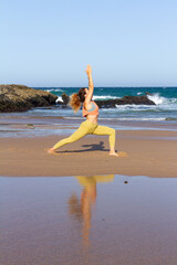 Strong yoga pose by a young woman in front of ocean with mirror reflection in the sand - Praia do Gincho - Portugal