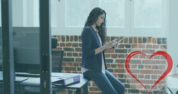Red heart icon against portrait of indian woman using digital tablet at office