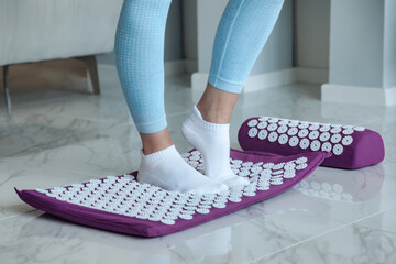Acupressure mat massage therapy. Woman feet standing on acupressure mat for self health massage in living room at home indoors - obrazy, fototapety, plakaty