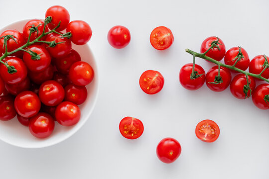 Top view of natural cherry tomatoes on branches in bowl on white background.