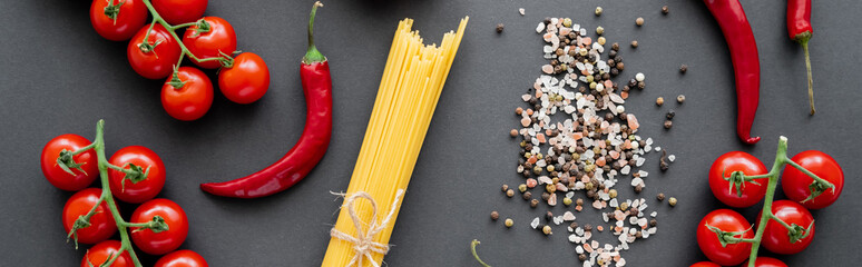 Top view of red ripe vegetables near raw pasta and spices on black background, banner.