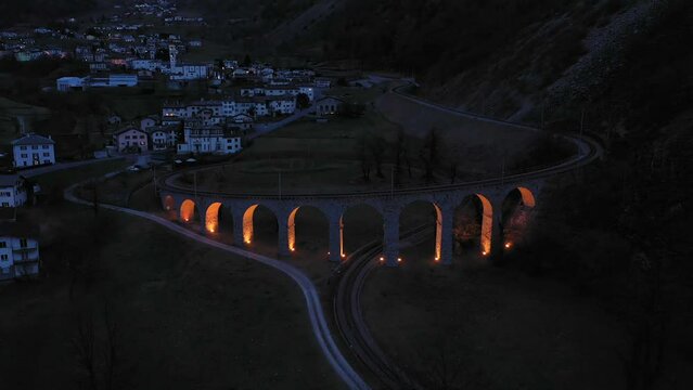 Illuminated Brusio Spiral Viaduct in Switzerland in the Evening. Bernina Railway. Swiss Alps. Aerial View. Orbiting