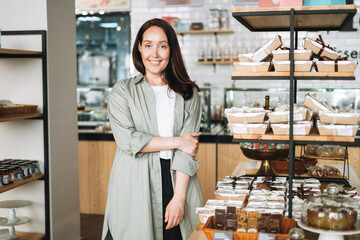 Adult smiling brunette business woman forty years with long hair in stylish shirt in cafe. Portrait of businesswoman manager in own small business in confectionery