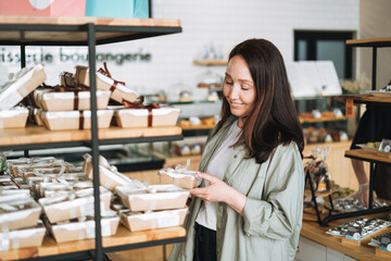 Adult smiling brunette woman forty years with long hair in stylish shirt choosing sweets in cafe,...