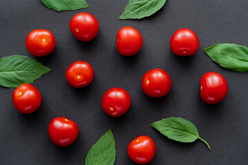 Top view of fresh cherry tomatoes and basil leaves on black background.