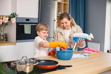 Little boy and his mother doing cleaning in a kitchen using a detergents