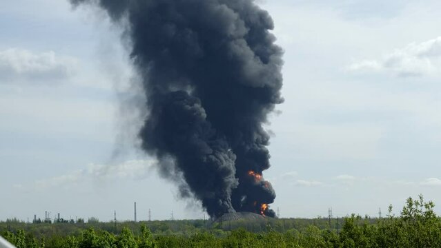 A giant fire and a high column of black smoke after the explosion at the oil storage. Huge clouds of black smoke against a blue sky. The concept of environmental pollution.