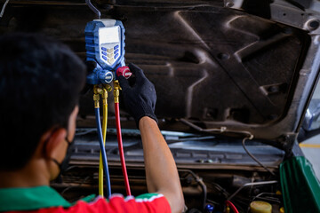 Asian male mechanic fills the car's refrigerant and check the car air conditioner compressor oil...