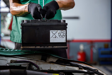 Close-up of a car mechanic in a service center picking up a new battery to replace the car. for...