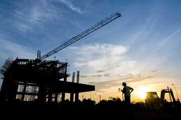 Silhouette of a male engineer standing at a construction site in the evening sunset. Construction engineers inspect quality and design plans of industrial construction projects.