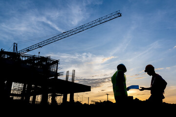 Fototapeta na wymiar Silhouette of a male engineer standing at a construction site in the evening sunset. A team of construction engineers talks to managers and construction workers at an industrial construction project.