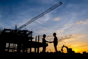 Silhouette of a male engineer standing at a construction site in the evening sunset. A team of...