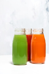 colorful vegetable juices in bottles on white table, vertical closeup