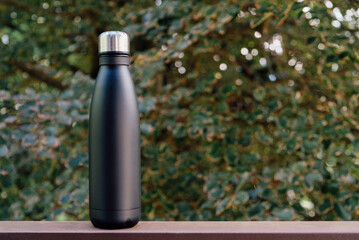 Reusable eco-friendly stainless steel thermo bottle against green nature summer background. Copy space for text. Zero waste, no plastic, sustainability. Bring your own water bottle concept.