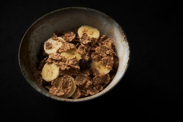 Bowl of granola with banana. Dark stone background. Close up. Copy space. 