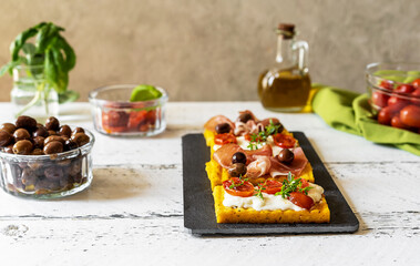 Italian antipasto - grilled polenta with soft cheese, tomatoes, herbs, speck and olive. White...