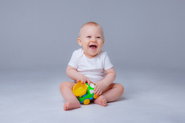 baby boy in a white bodysuit is sitting playing  with toy cars on white background