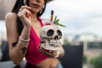 Happy beautiful young woman enjoys a relaxing time on the terrace of a bar with skull glass