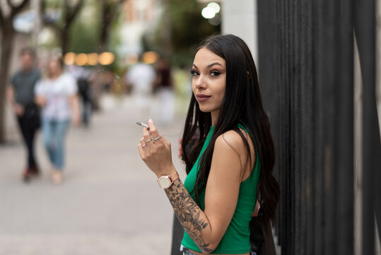 Beautiful woman poses outdoors on the city street while smoking a cigarette