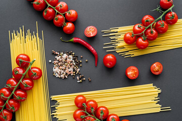Flat lay of natural vegetables and spaghetti with spices on black background.