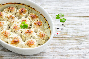 Rustic cream parmesan meatballs in baking dish on wooden background. Top view, copy space, flat lay.