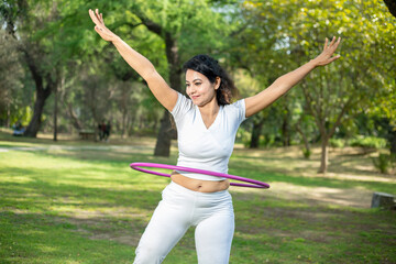 Beautiful Indian young woman doing workout with hula hoop in the park outdoor, Happy asian female waist building and weight loss.sports and Fitness concept.