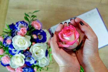 Flatlay. Female hands hold a rose flower. Notebook, diary with a pen on a wooden table near a...