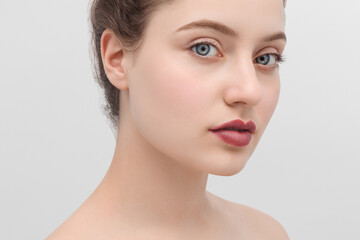 Close up shot of a beautiful brunette girl with blue eyes and nude colored lipstick on a light gray background.