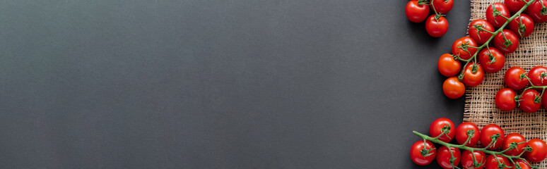 Top view of natural cherry tomatoes on sackcloth on black background, banner.