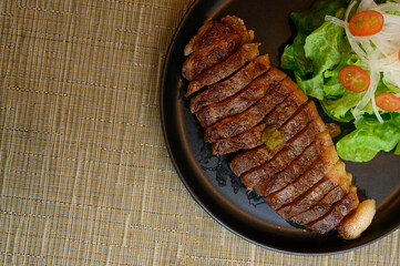 Beef or pork steak with vegetable salad is placed in a black plate.