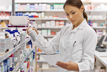 Preparing customer prescriptions. Shot of an attractive young pharmacist checking stock in an aisle.