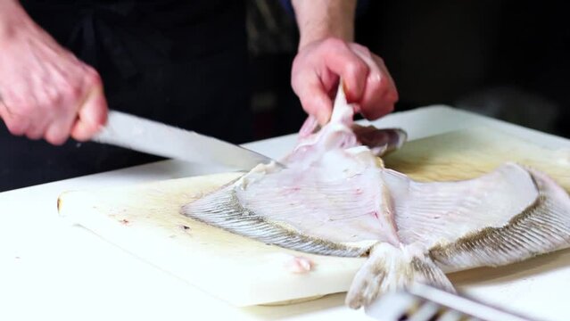 A fish vendor cleans up a nice monkfish with a kitchen knife, over a white cutting board. He cuts the head
