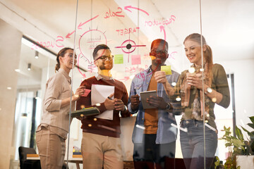 Young marketing team cooperating while making mind map on glass wall in office.