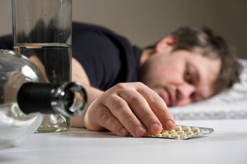 A man lies on a bed after an alcohol party, holding hangover pills in his hand
