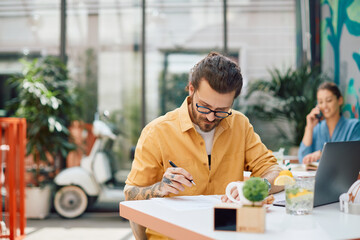 Fototapeta premium Young businessman going through paperwork while working in cafe,