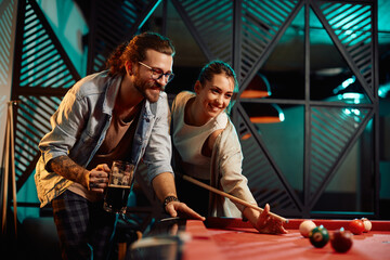 Young happy couple enjoy while playing billiard in pool hall.