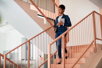African American businesswoman with touchpad walks down the stairs. - obrazy, fototapety, plakaty