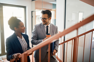 Happy business colleagues talk while drinking coffee and walking up the stairs.