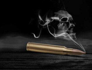 Bullet with skull shaped smoke on black wooden table