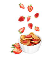 Fresh berries falling into bowl with tasty pancakes against white background