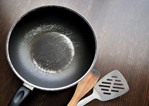 Old scratched non-stick pan on wood table. Teflon pan peeling off. Copy space is on the right side. 