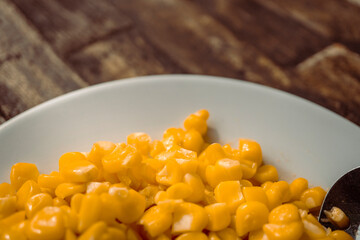 Macro of sweet corn over the white plate on wooden table. The photo is perfect for food background, brochure and pamphlet advertising.