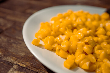 Macro of sweet corn over the white plate on wooden table. The photo is perfect for food background, brochure and pamphlet advertising.