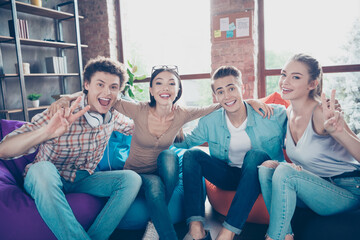 Photo of funny charming groupmates sitting dormitory beanbags embracing showing v-signs indoors...