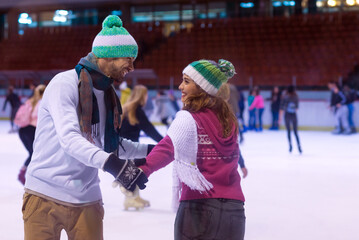 Smiling young couple ice skating in the public ice rink in winter