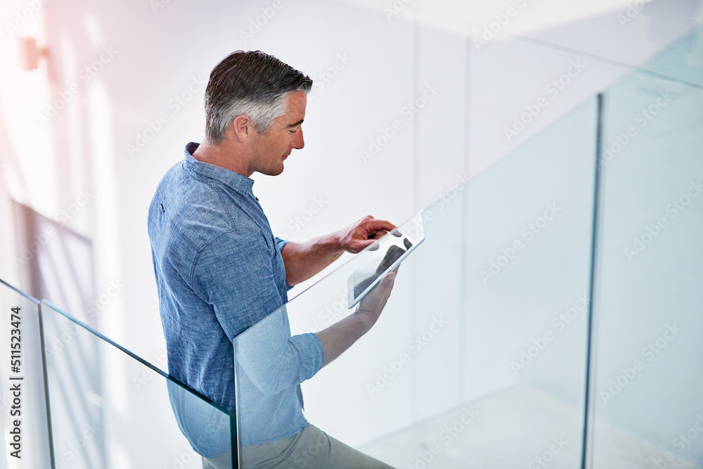 Poster keeping up with the pace of modern business. shot of a mature businessman using a digital tablet on 