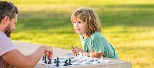 Father and son play chess outdoor, banner poster with copy space, happy family of dad and son boy playing chess on table in park outdoor, chess competition