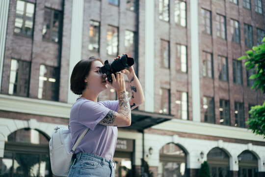 Young Girl Photographer Takes Pictures of City Architecture. Tattooed Girl with Camera Takes Pictures in City Center
