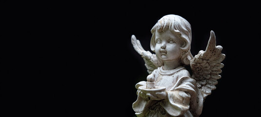 old statue of angel baby with candle on abstract black background. concept of faith, Christianity,...