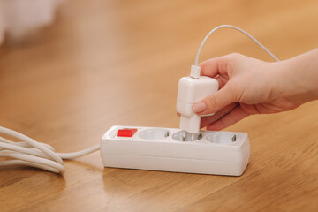 Woman pluging the wire into white extension cord. Close up of female hand put cabel